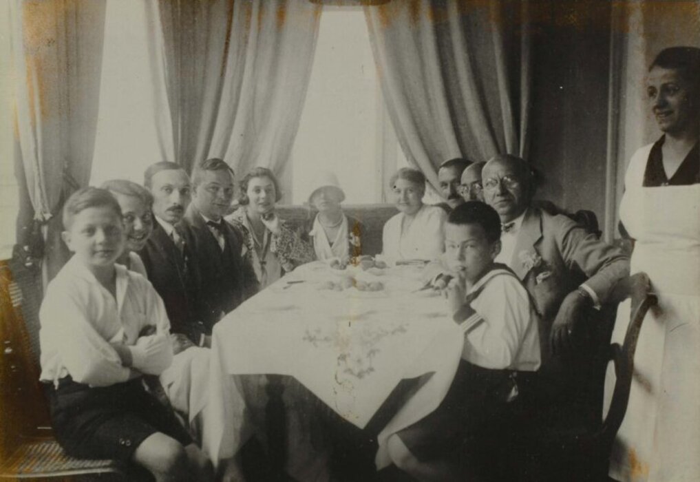 Ein schwarz weiß Foto von Familie Neumann. Familientreffen, ca. 1920 (?); Wally Grünbaum, geb. Neumann (2.v.l.), Lea Neumann (7.v.l.) und Leo Neumann (10. v.l.). Sie sitzen alle um einen großen Esstisch herum.