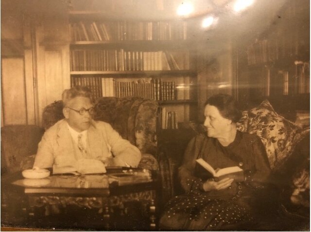 Man sieht Olga und Gustav Langendorf in ihrer Wohnung im Prag der 1930er Jahre sitzen. Sie sitzten in Sesseln vor Buchschränken und haben beide Bücher zum lesen in der Hand