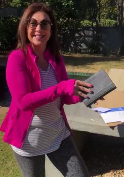 Man sieht Frau Debbie Meyer beim Auspacken des Pakets in einem Park in Johannesburg. Sie wirkt sichtlich erfreut über das Gesangbuch Ihrer Großmutter. Welches ihr von der HFJS zugesandt wurde.