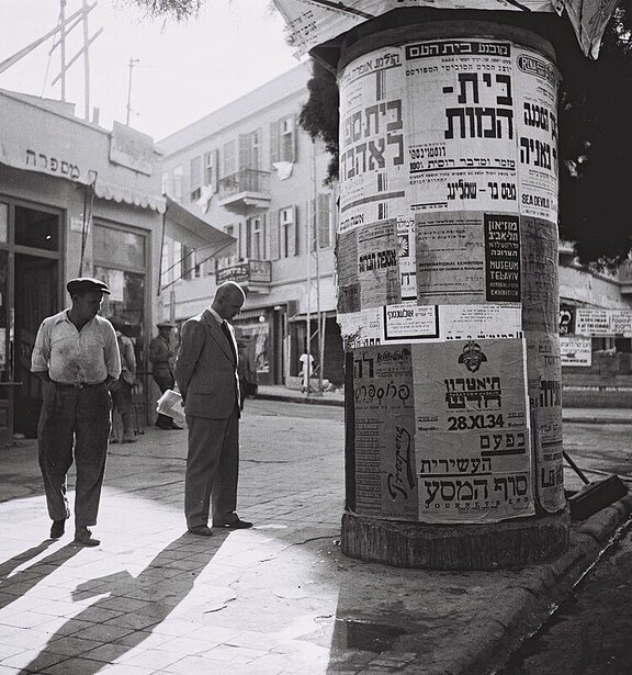 Ein Mann schaut auf Billboard mit Postern auf hebräisch.